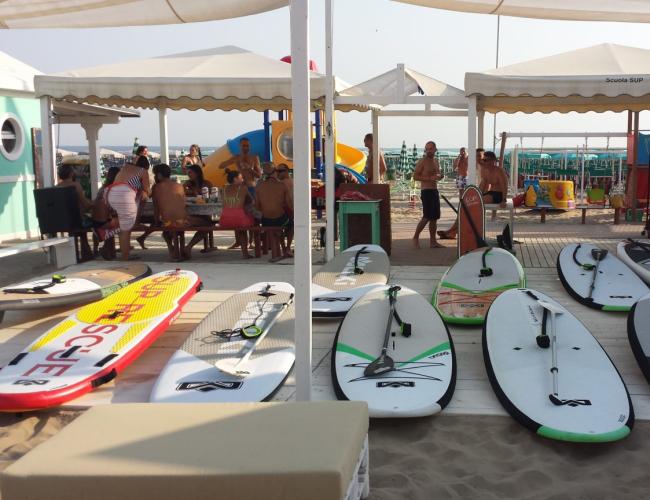 Tavole da SUP sulla spiaggia, persone sotto i gazebo.